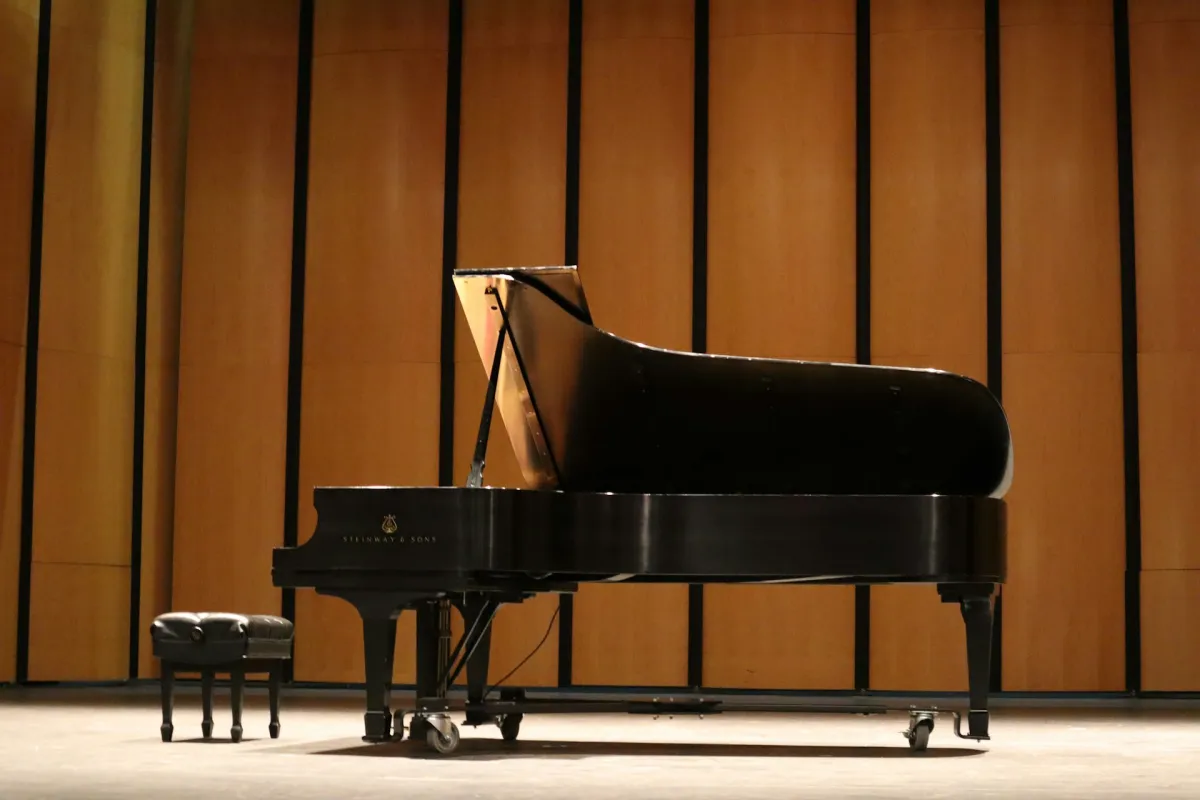 A concert grand piano and stool on a recital stage